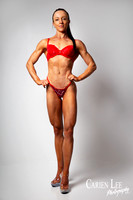 Full-length female fitness physique portrait in red posing attire against a grey studio background